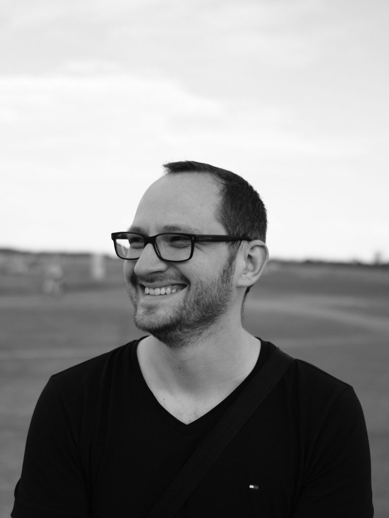 Ein Mann mit Brille steht auf einem großen Feld und lächelt.